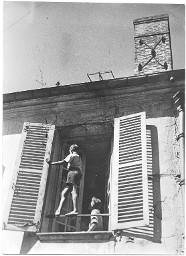 Aussenansicht eines Fensters mit offenen Fensterläden: Ein Junge balanciert auf einer quer zum Fensterrahmen angebrachten Eisenstange, ein zweiter Junge steht im Zimmer direkt beim Fenster, 1930er/1940er Jahre (Vemerk Rückseite: "Hans Affeltranger, Arthur Küng")