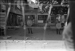 "AJZ-Schliessung" - Polizeieinsatz aufgrund der Räumung des autonomen Jugendzentrums / Blick durch den Maschendrahtzaun auf zwei Polizeibeamte, 04.09.1980