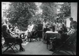 Pensionärinnen auf der Terasse eines Heimes, manche sitzend, einige Bücher lesend, möglicherweise eine Lesung, Garten im Hintergrund, um 1930