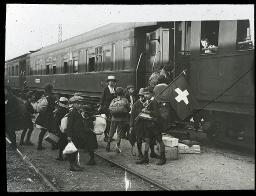 "Buchs, Bahnhofwerk", Kinder steigen über Gleise in einen Zug ein, ein Knabe hält eine Schweizerfahne hoch, Betreuerin überwacht die Szene, Kinder schauen aus dem Zug, um 1925