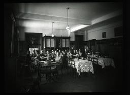 "Herisau, Marthaheim", Pensionärinnen im Esszimmer vor gedecktem Tisch, im Hintergrund wird ein grosser Kochtopf hereingetragen, vermutlich kurz vor dem Abendessen, um 1925