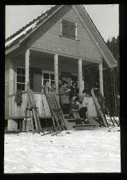 "Zürich, Mädchenklub Schanzengraben", Mädchen auf der Treppe zu einer Holzhütte, vermutlich Tee oder Kaffee trinkend, daneben mehrere Skis, Wiese mit Schnee bedeckt, um 1935