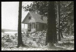 "Wochenendhäuschen", an Waldrand oder an Waldichtung gelegene Holzhütte, Jungbäume, vermutlich Tannen, vor der Hütte, schneebedeckter Boden, um 1935