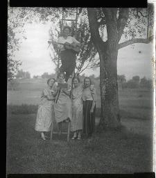 "Töchterheim Jakobstrasse, Zürich", fünf junge Frauen unter einem Baum auf einer Wiese, eine spielt auf einer Leiter Gitarre, die anderen vier singen vermutlich mit, eine davon ein Liederbuch in der Hand haltend, um 1930