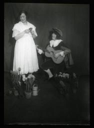 "Zürich, Töchterheim Jakobsweg", vermutlich eine Theatervorstellung, zwei Frauen spielen eine Szene, eine davon im weissen Kleid mit Pflanzen, die andere als Musiker verkleidet mit einer Gitarre, um 1930