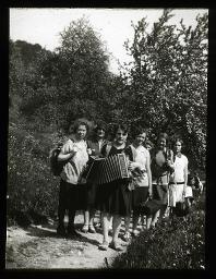 "Zürich, Neues Töchterheim", mehrere Mädchen posieren auf Wanderweg für Kamera, eines mit Akkordeon, im Hintergrund Bäume und Büsche, um 1930