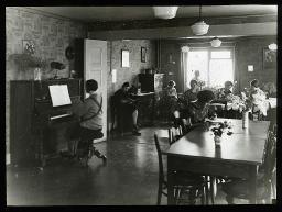 "Zürich, Neues Töchterheim", mehrere junge Frauen und Mädchen im Speisesaal oder Aufenthaltsraum, am Lesen und Klavierspielen, vereinzelt am Stricken, um 1925